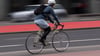 Ein Fahrradfahrer mit Helm fährt über einen Radweg an der Straße.
