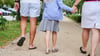 Ein Vater und eine Mutter halten die Hände ihrer Tochter, während sie auf einem Gehweg gehen.