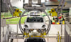 Die Karosse eines Porsche E-Macan schwebt in einem Drehgehänge durch das Leipziger Porsche Werk. 