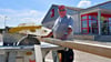 Bauarbeiter Roland Melzer sägt auf der Baustelle Holzbalken auf das gewünschte Maß, während seine Kollegen dabei sind, das Fundament zu legen.
