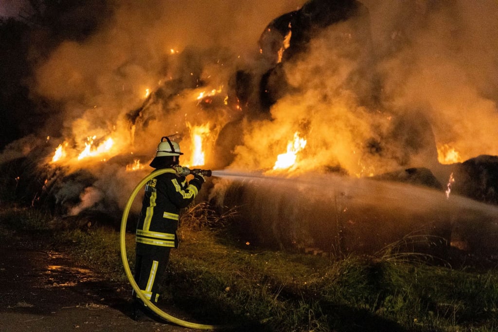 Ein Feuerwehrmann löscht brennende Strohballen.