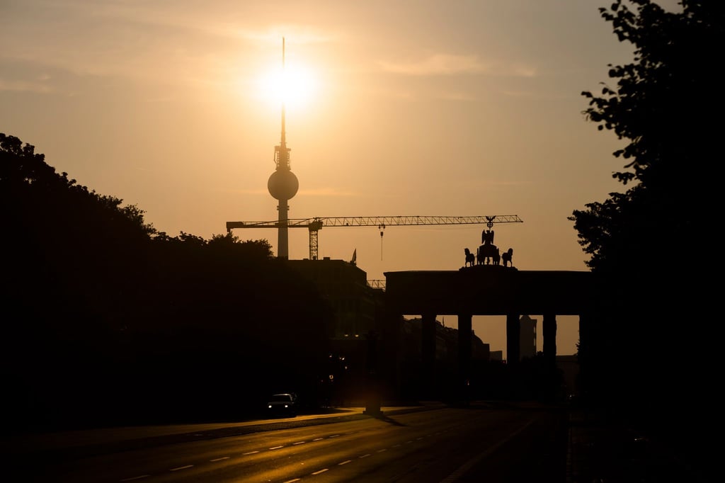Das Brandenburger Tor und der Fernsehturm sind im Gegenlicht der aufgehenden Sonne zu sehen.