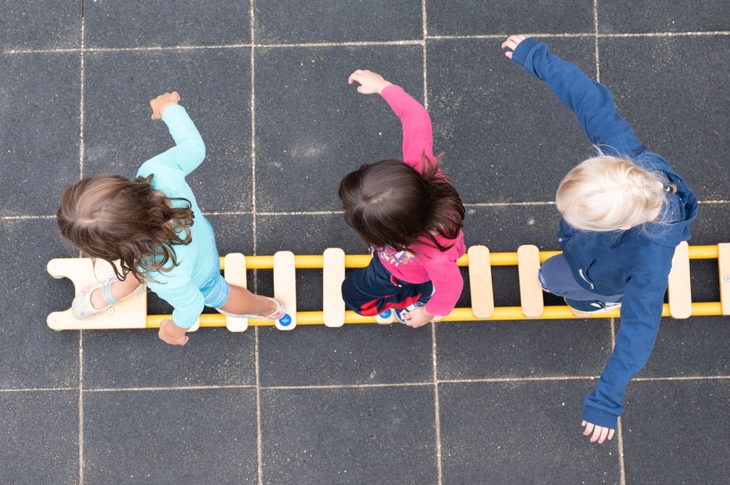 Kinder balancieren während eines Pressetermins auf dem Spielplatz einer Kindertagesstätte auf einem Brett.