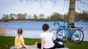 Eine Frau und ein Kind sitzen bei sonnigem Wetter am Ufer vom Hufeisensee in der Region Hannover.