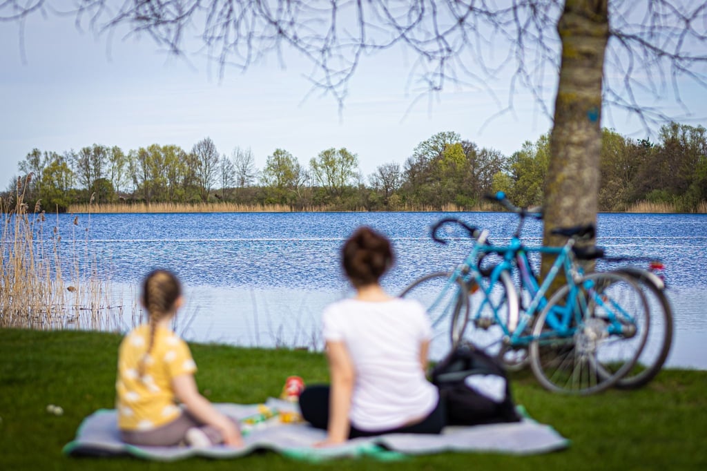 Eine Frau und ein Kind sitzen bei sonnigem Wetter am Ufer vom Hufeisensee in der Region Hannover.