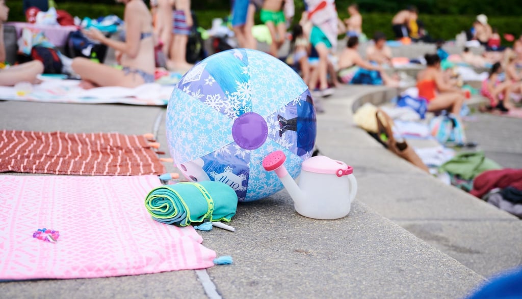 Ein Wasserball und Handtücher liegen in einem Schwimmbad am Beckenrand.