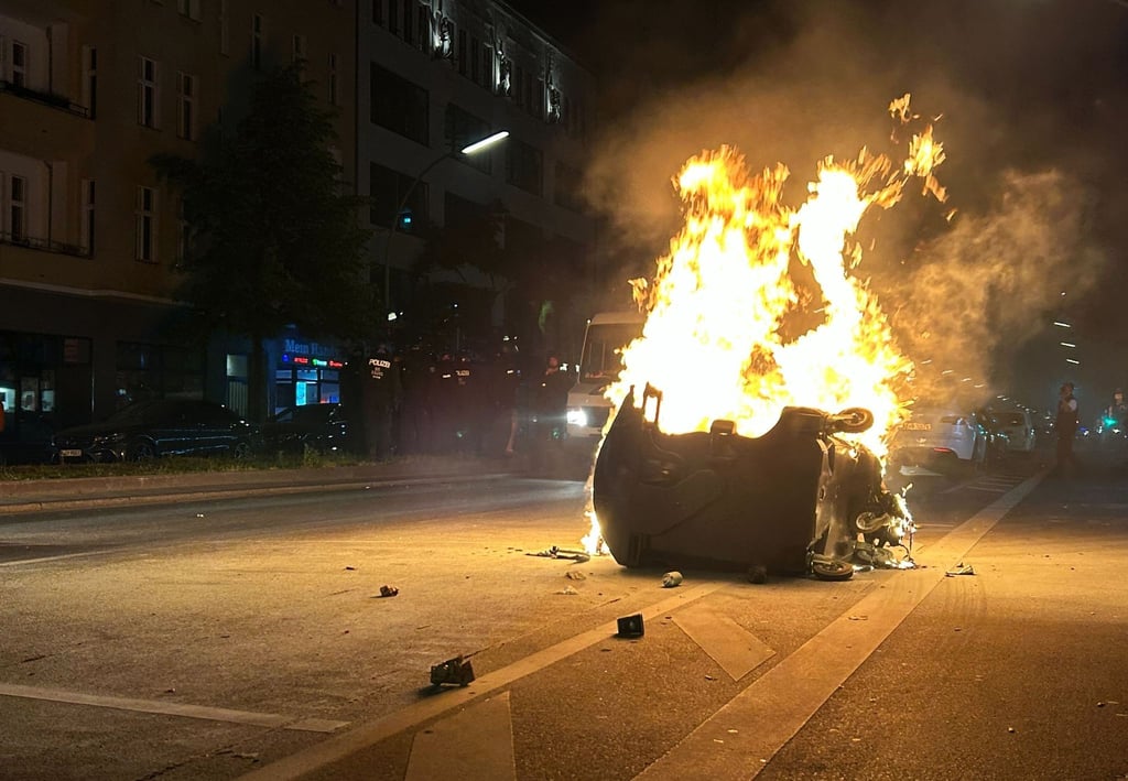 Während eine Mülltonne auf dem Kottbusser Damm im Stadtteil Neukölln brennt, sind Polizisten im Einsatz.
