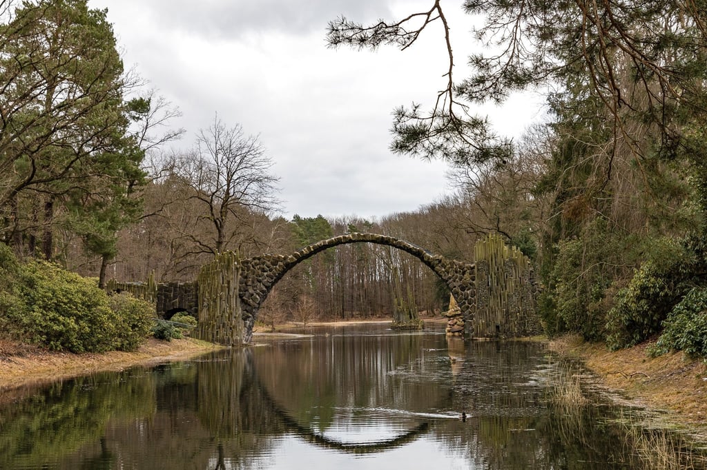 Die Rakotzbrücke aus Basaltsteinen im Kromlauer Rhododendronpark spiegelt sich bei bedecktem Wetter im Rakotzsee.