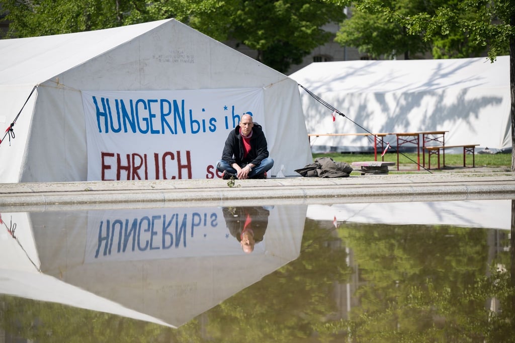 Wolfgang Metzeler-Kick sitzt am neuen Standort des Hungerstreik-Camps des Bündnisses „Hungern bis ihr ehrlich seid“ im Regierungsviertel vor einem Banner.