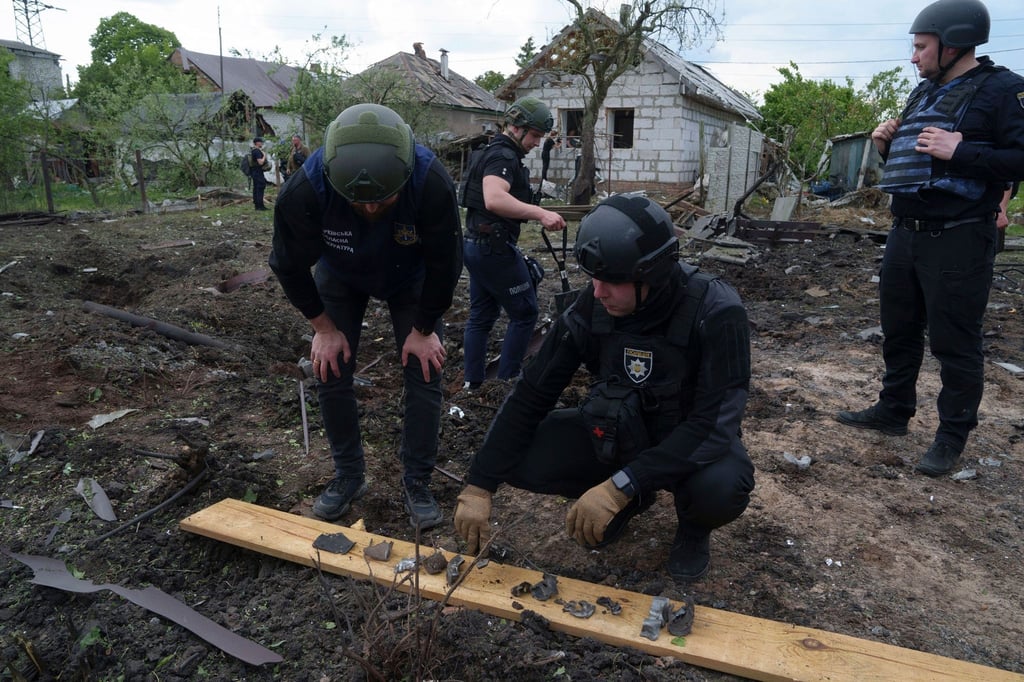 Ein ukrainischer Polizeibeamter und ein Staatsanwalt für Kriegsverbrechen inspizieren Bruchstücke einer Gleitbombe vor einem beschädigten Haus nach einem russischen Luftangriff auf ein Wohnviertel.