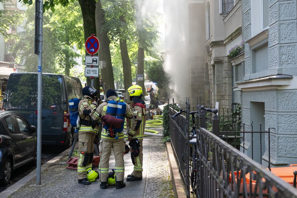 Feuerwehrleute stehen mit Atemschutz vor einem Gebäude, aus dem Rauch quillt.