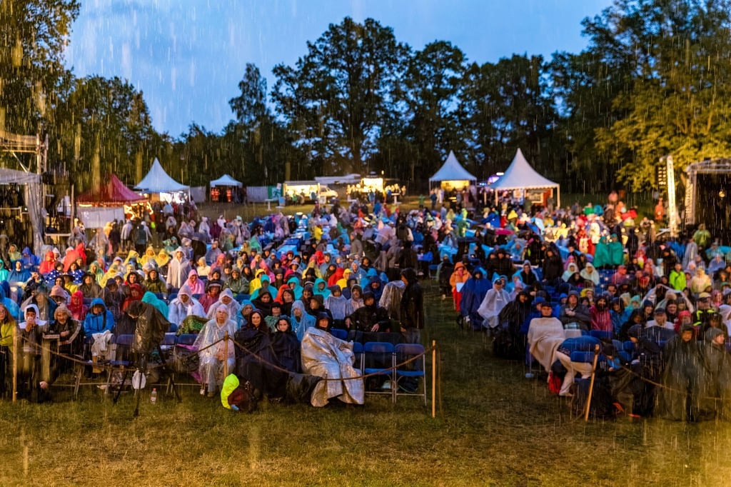 Besucher der Premiere des Stückes „Jan a gluka - Die sagenhafte Suche nach Glück“, sitzen im Regen vor der Freilichtbühne am Bismarckturm.