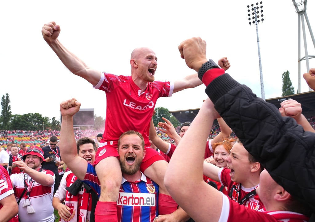 Maximilian Krauß von Cottbus und seine Mitspieler bejubeln nach Schlusspfiff und Platzsturm den Aufstieg mit den Fans.