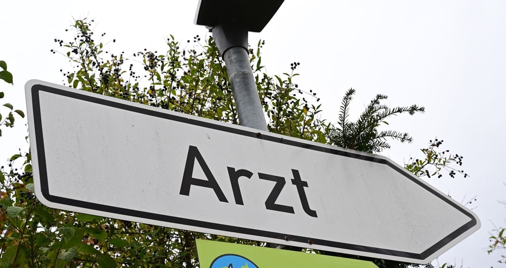 Ein Schild mit der Aufschrift Arzt steht an einer Straße.