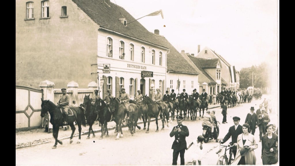 Das Bild zeigt einen Umzug zum 1. Mai Ende der 1920er Jahre. Er befindet sich vor der Gaststätte "Deutsches Haus", in dem heute direkt am Platz des Friedens "Amarjit" seine Räumlichkeiten hat.