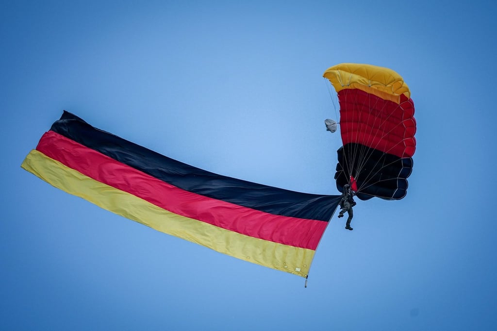 Fallschirmspringer der Bundespolizei mit Deutschlandfahne über dem Staatsakt zu „75 Jahre Grundgesetz“.