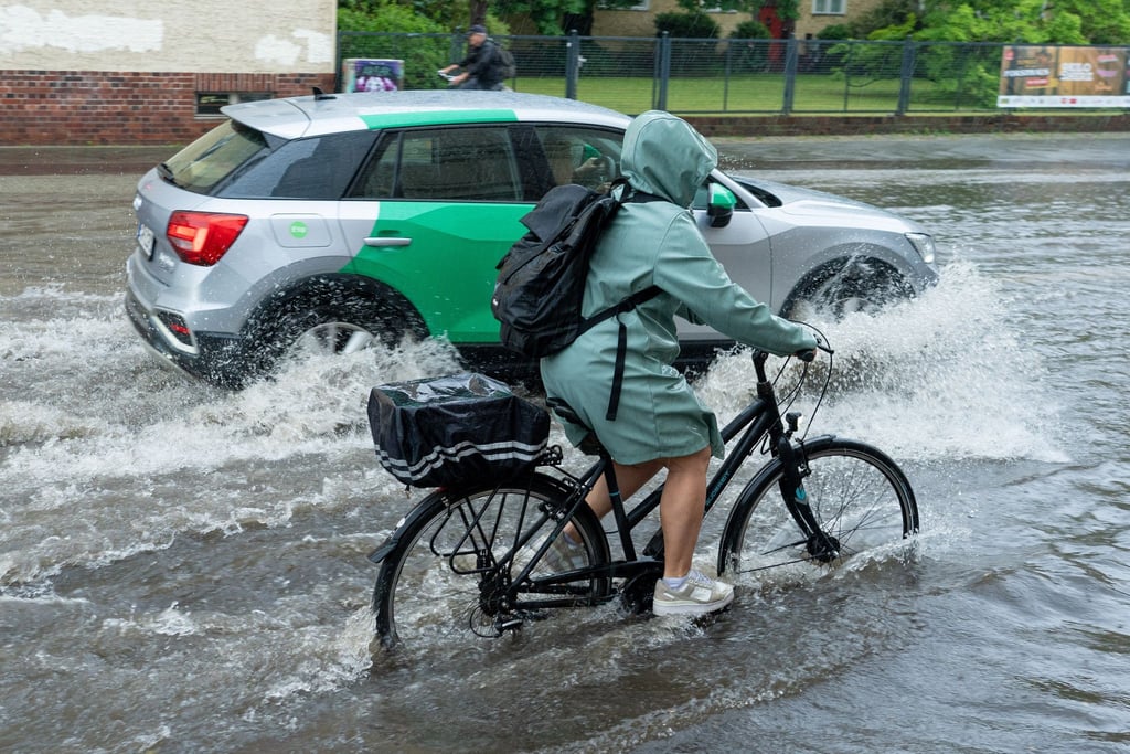 Eine Radfahrerin und ein Auto fahren im Schritttempo durch die überflutete Zeppelinstraße.