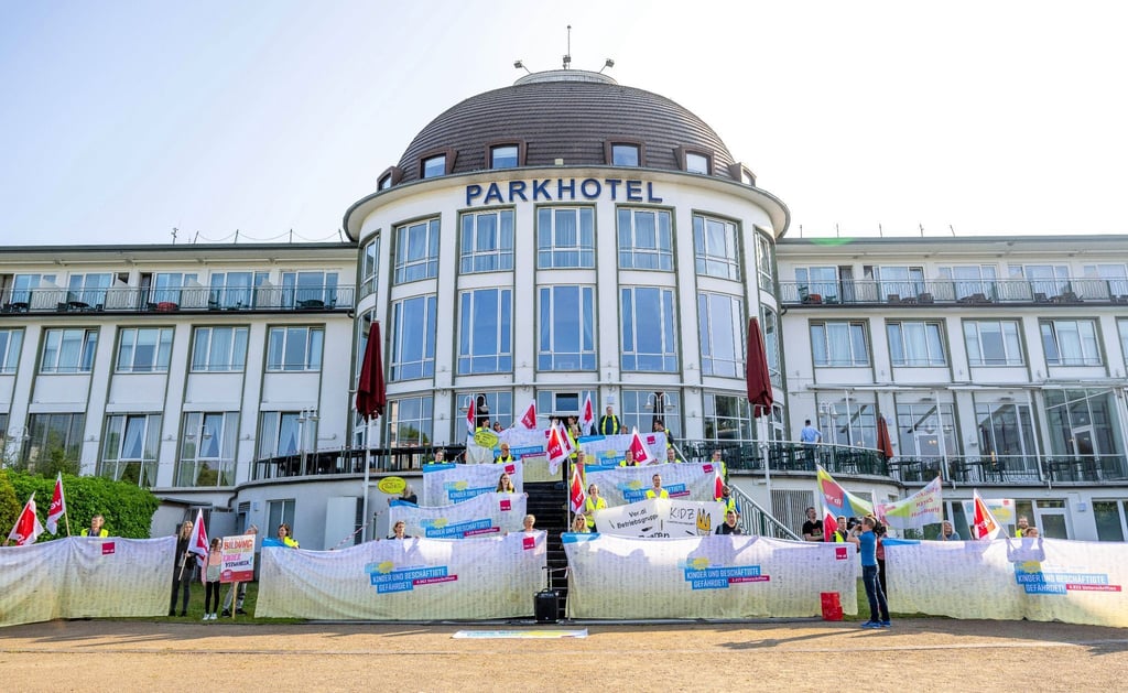 Kita-Beschäftigte stehen mit Fahnen vor dem Hotel, in dem die Familienministerkonferenz stattfindet.