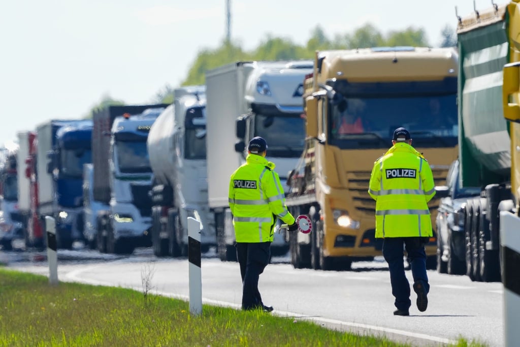 Polizeibeamte stehen kurz vor der Abfahrt zum Parkplatz an der Autobahn und winken Lastwagen aus dem fließenden Verkehr.