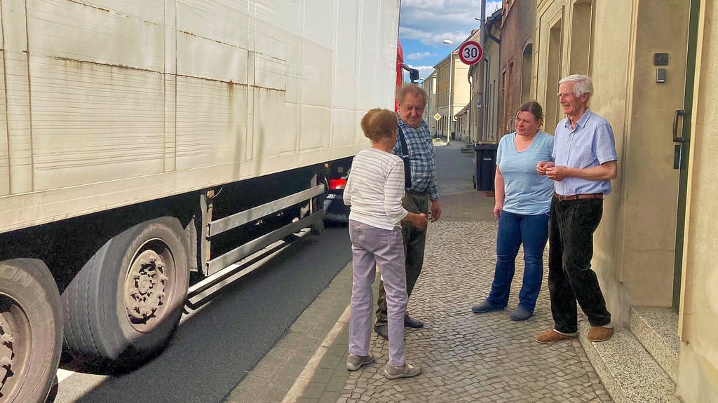 Renate Raabe (li.) ist auf dem schmalen Gehweg im Gespräch mit anderen Anwohnern. In umittelbarer Nähe fahren die Lkw vorbei.