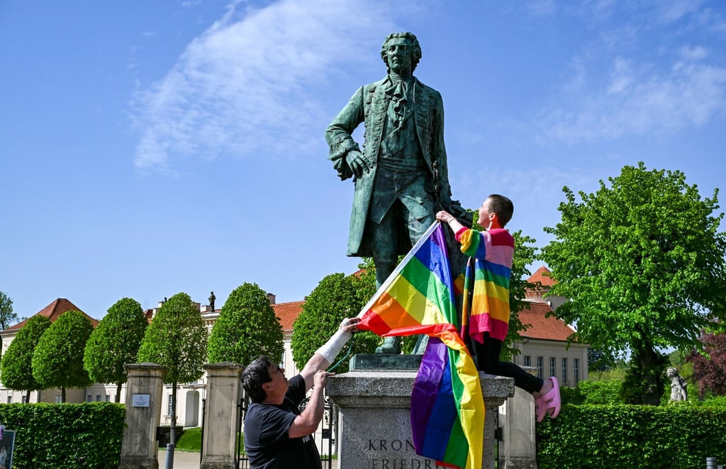 Am Denkmal von Kronprinz Friedrich zeigen der Politiker Freke Over und Marie von der Vorbereitungsgruppe des ersten "Christopher Street Day" (CSD) in Rheinsberg die Regenbogenfahne.
