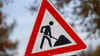 Ein zerkratztes Schild Gefahrzeichen Arbeitsstelle (Zeichen 123) mit dem Piktogramm eines Bauarbeiters zur Beschilderung einer Baustelle.