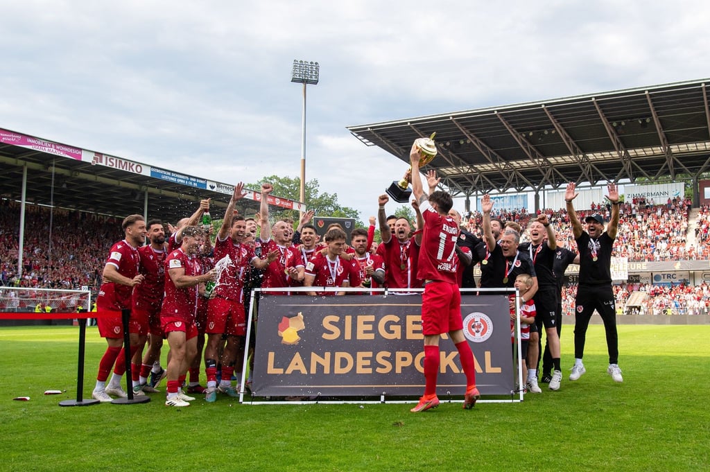 Jonas Hildebrandt von Energie Cottbus hält die Siegertrophäe in die Höhe und bejubelt den Landespokalsieg.
