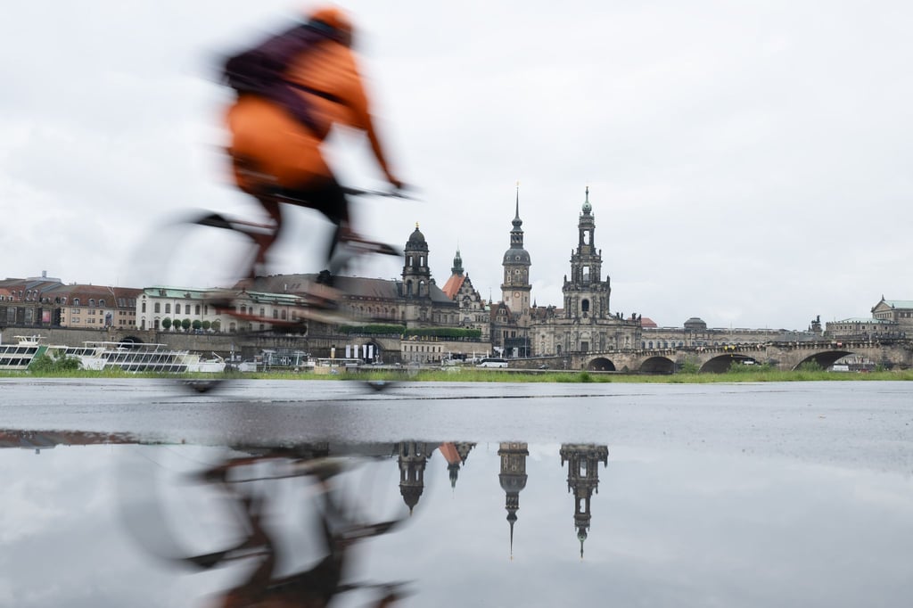 Ein Radfahrer fährt am Ufer entlang. Die Kulisse der Altstadt spiegelt sich in einer Pfütze am Ufer der Elbe.