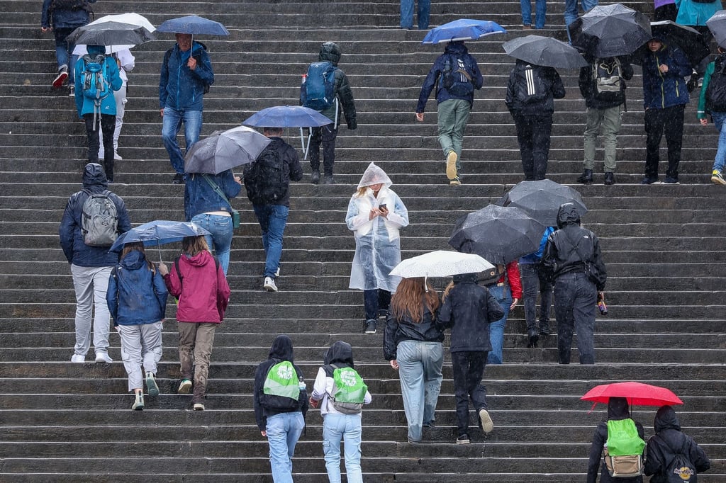 Besucher des 103. Deutschen Katholikentages gehen bei strömendem Regen über die Domstufen.
