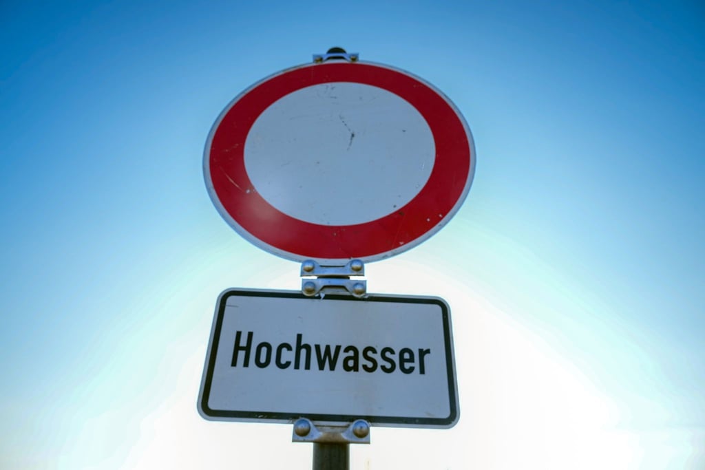 Ein Verkehrsschild für „Durchfahrt verboten“ mit dem Zusatz „Hochwasser“ steht am Ufer eines Flusses.