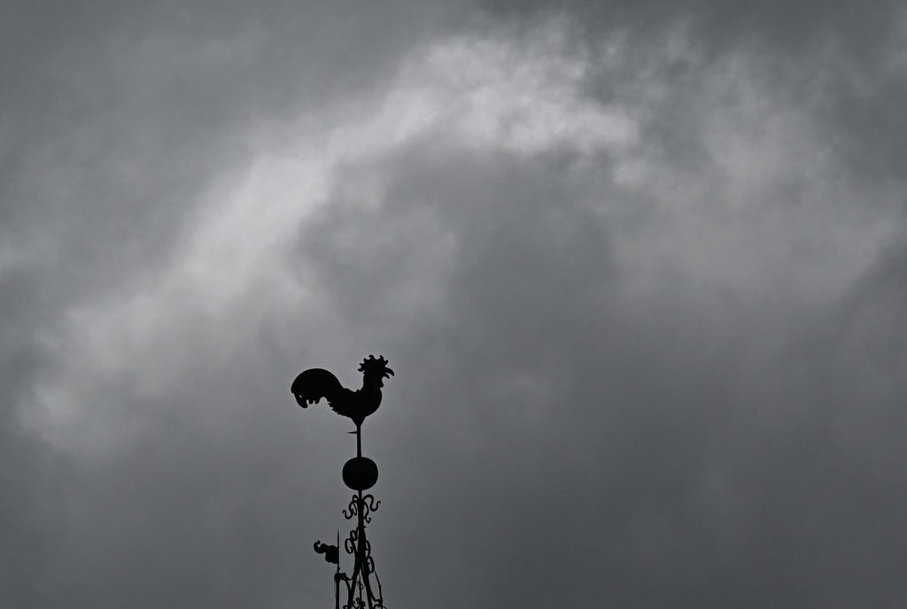 Über einem Wetterhahn schweben dunkle Regenwolken.
