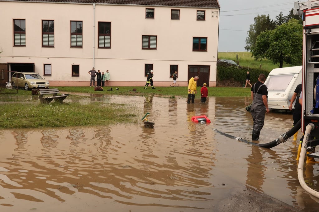 Nach einem Starkregen pumpen Einsatzkräfte der Feuerwehr auf einen Dorfplatz das Wasser ab.