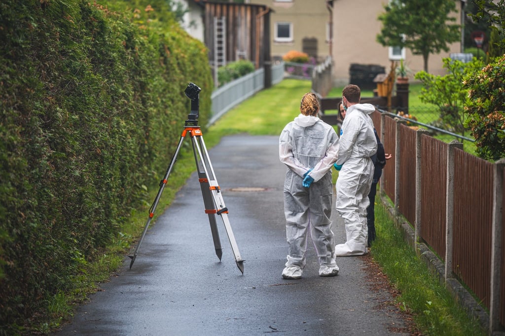 Polizeibeamte stehen an einem Tatort auf der Straße. In einem nahe gelegenen Haus war es zu einem Gewaltverbrechen mit drei Toten gekommen.