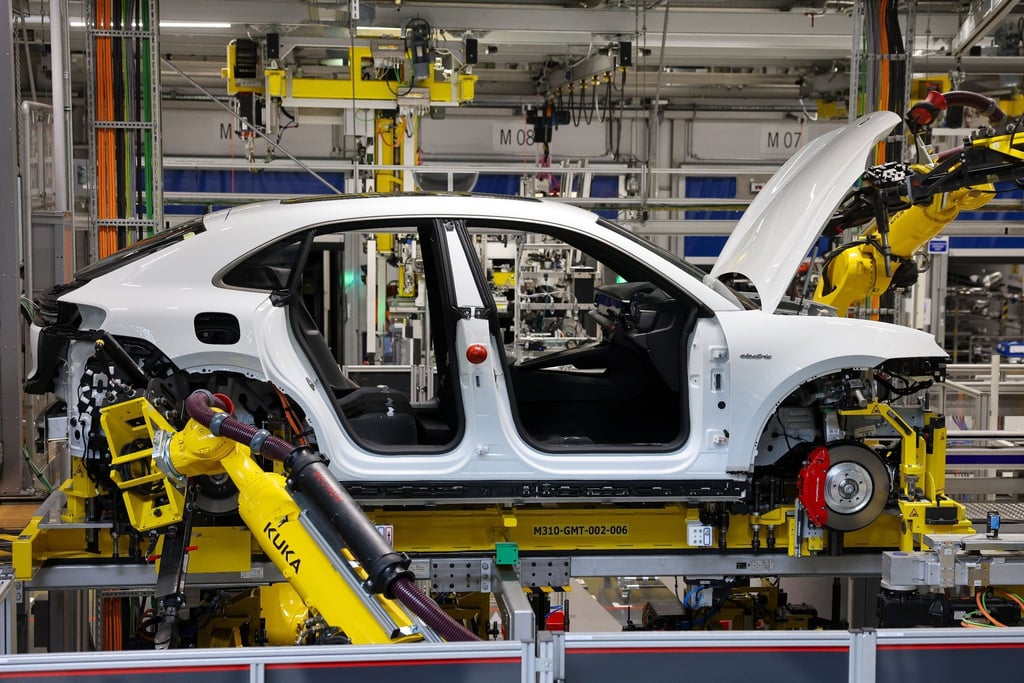 Industrieroboter arbeiten an einem vollelektrischen Porsche Macan nach der Hochzeit (der Verbindung von Fahrwerk und Motor mit der Karosse) im Werk Leipzig.