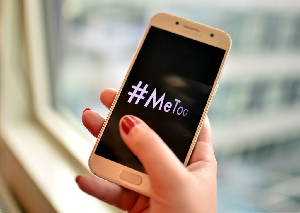 Eine junge Frau hält ein Smartphone mit dem Hashtag "#MeToo" in der Hand.