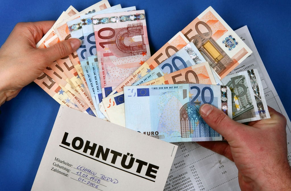 Zwei Hände stecken symbolisch Euro-Geldscheine in eine Lohntüte.