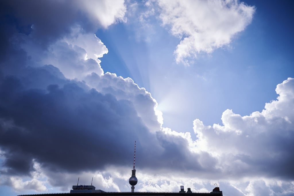 Die Sonnenstrahlen kommen hinter einer dunklen Wolke über dem Fernsehturm hervor.