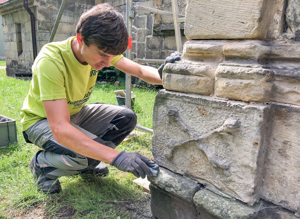 Jannis Ehrich, sonst bei der Außenstelle des Landesamtes für Denkmalpflege und Archäologie in Heyrothsberge im Einsatz, entfernt mit einem Schleifstein Ablagerungen am Sandstein des Mausoleums.