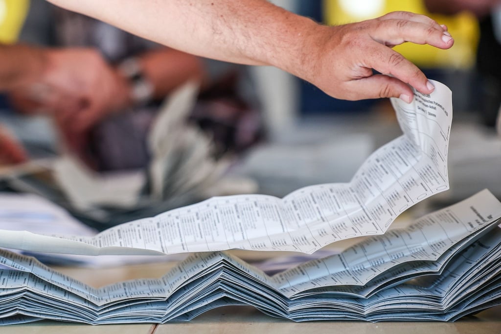 Ein Wahlhelfer legt Stimmzettel zur Stimmenauszählung der Briefwahlstimmen zur Europawahl auf einem Stapel.