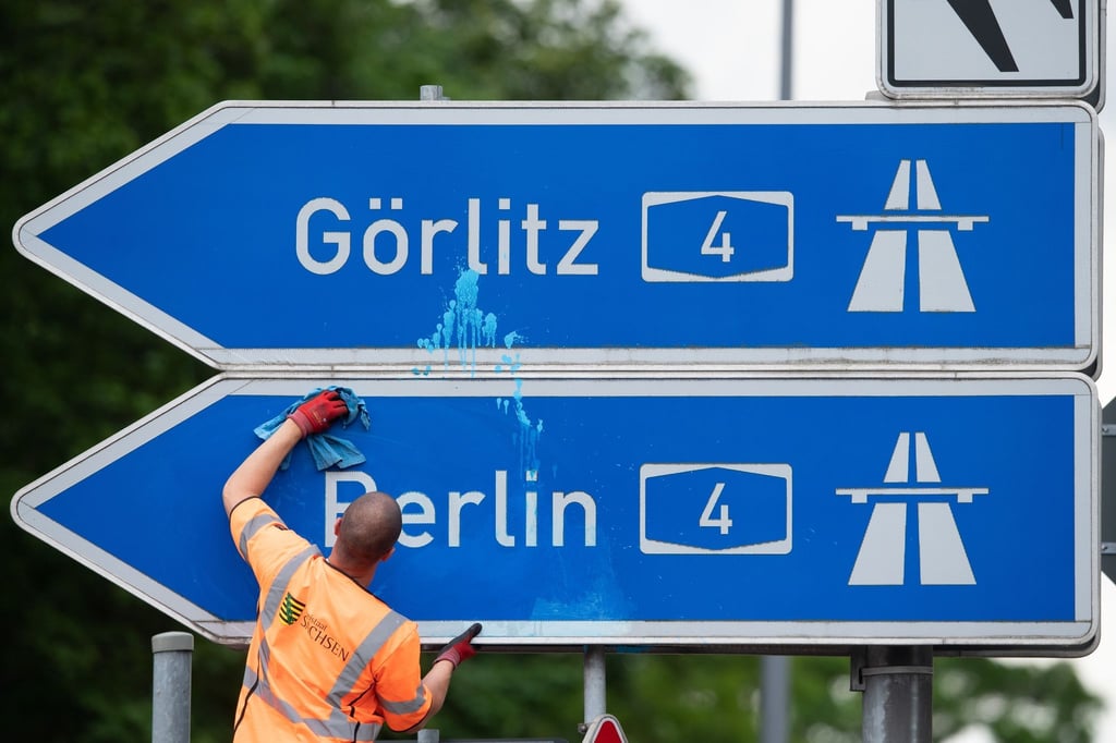 Ein Mann reinigt das blau-weiße Schild der Autobahnauffahrt A4 Richtung Berlin und Görlitz.