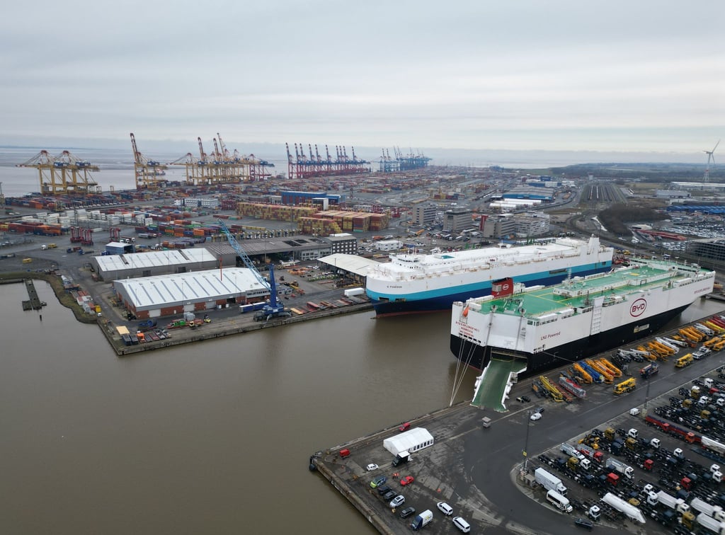 Auf dem Bild ist das Autoterminal in Bremerhaven zu sehen, im Hintergrund stehen Kräne des Containerterminals.