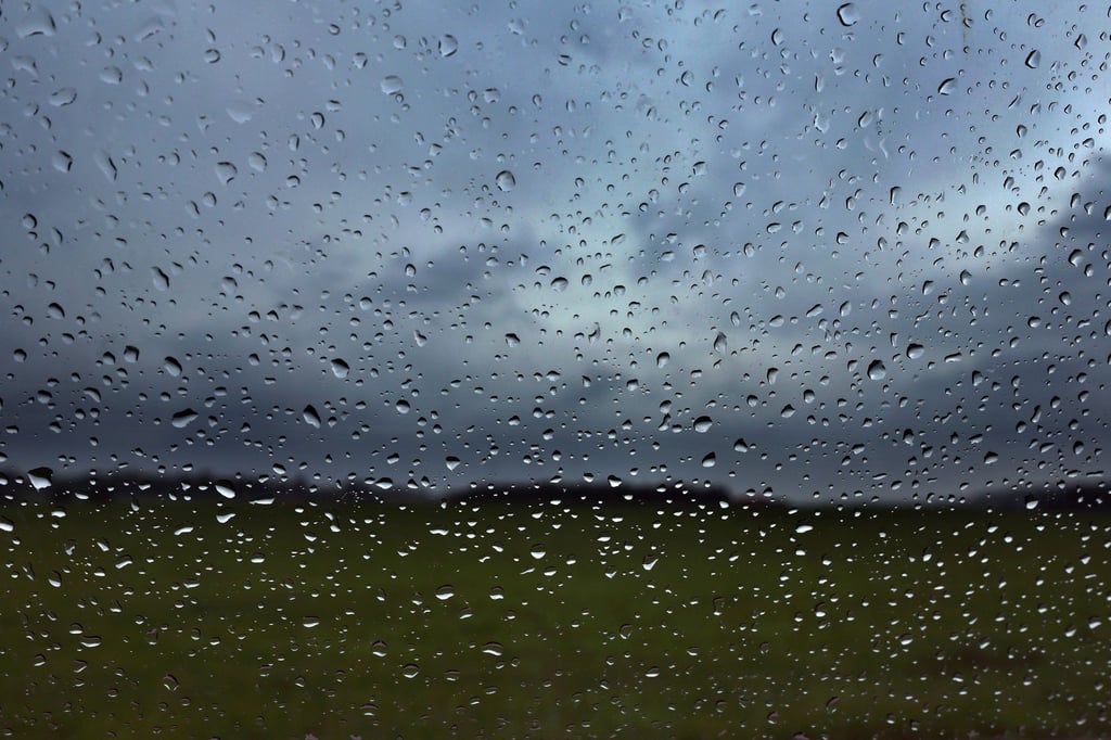 Eine Autoscheibe ist vor dunklen Wolken mit Regentropfen bedeckt.
