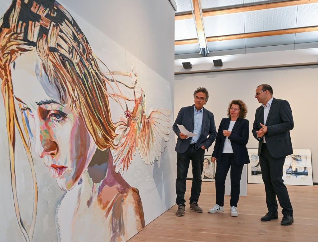 Frank Mangelsdorf (l), Jury-Vorsitzender, Heike Kramer, Geschäftsführerin der Stiftung Schloss Neuhardenberg und Tobias Dünow (SPD), Kulturstaatssekretär, stehen neben einem Gemälde von Cornelia Schleime.