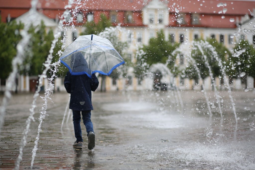 Ein Kind geht mit einem Schild bei Regenwetter durch ein Wasserspiel auf dem Domplatz.