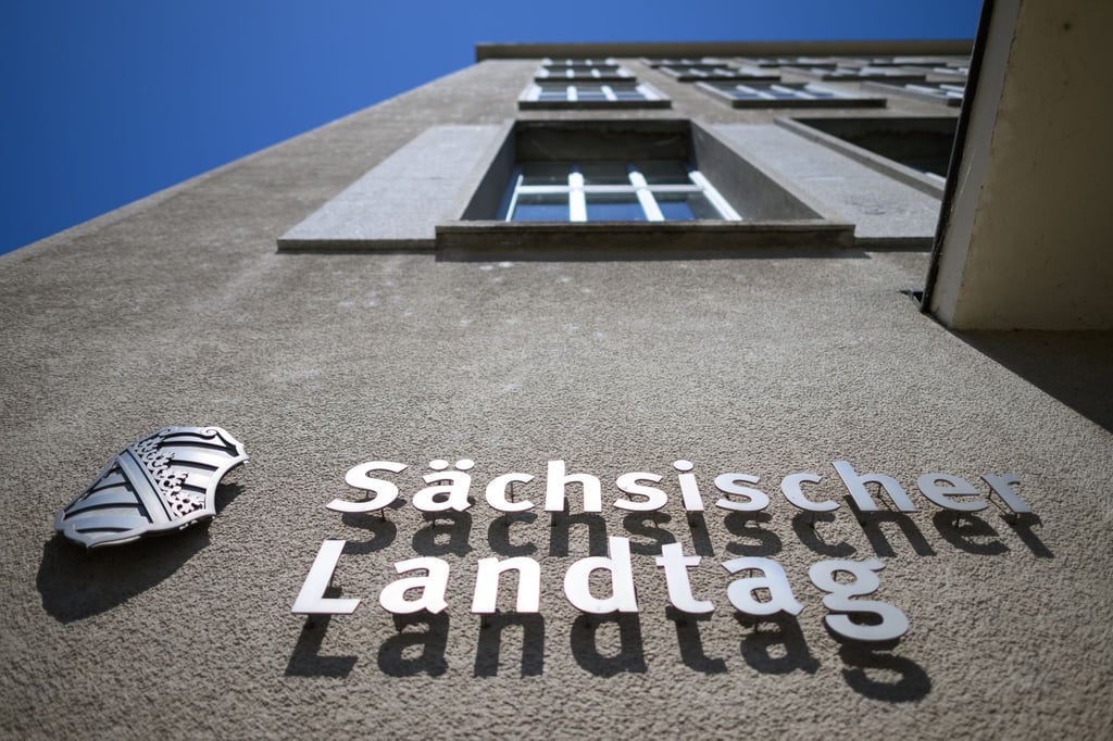Sächsischer Landtag und eine Wappen von Sachsen sind an der Fassade am Altbau des Parlamentsgebäudes montiert.