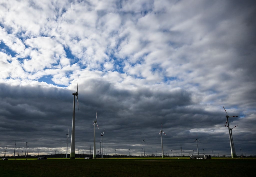 Windräder werden bei wolkigem Himmel kurzzeitig von der tiefstehenden Sonne beleuchtet.