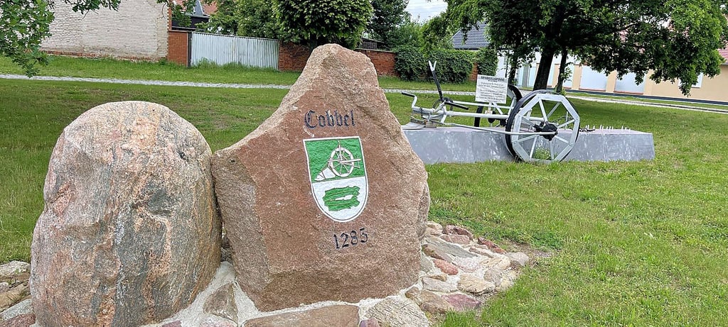 Das Denkmal auf dem Dorfplatz von Cobbel mit Spargelspinne im Hintergrund und dem Findlingsensemble ist nun komplett.