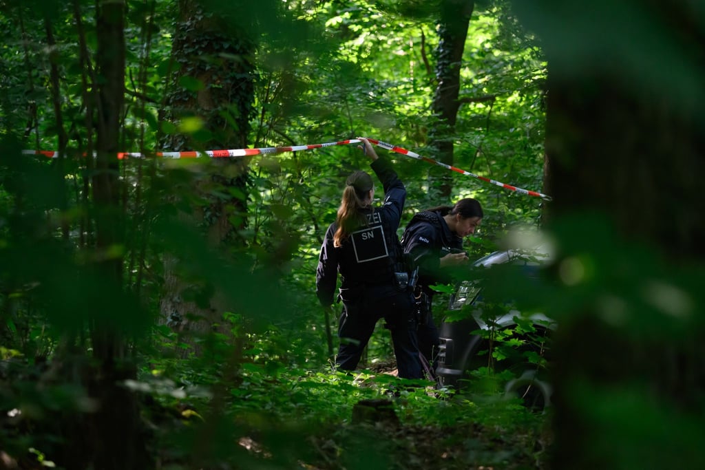 Eine Polizistin hält in einem Wald Absperrband hoch.