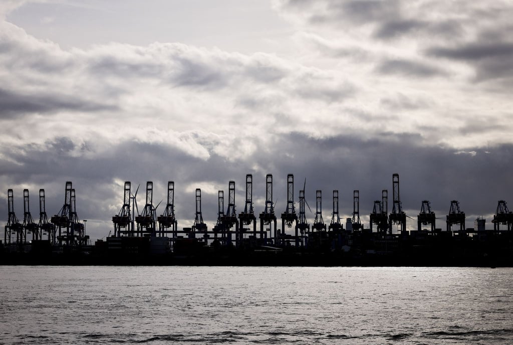 Hochgeklappte Containerbrücken sind als Silhouetten im Hafen an der Elbe zu sehen.