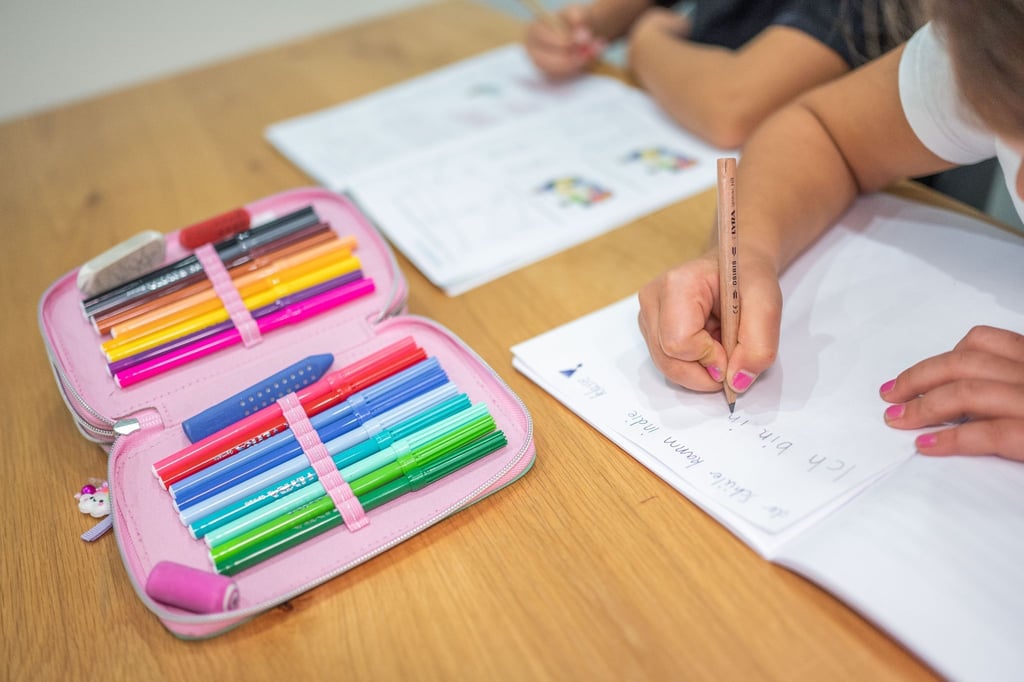 Ein Grundschüler und eine Grundschülerin sitzen in einem Wohnzimmer am Tisch und erledigen Schulaufgaben.